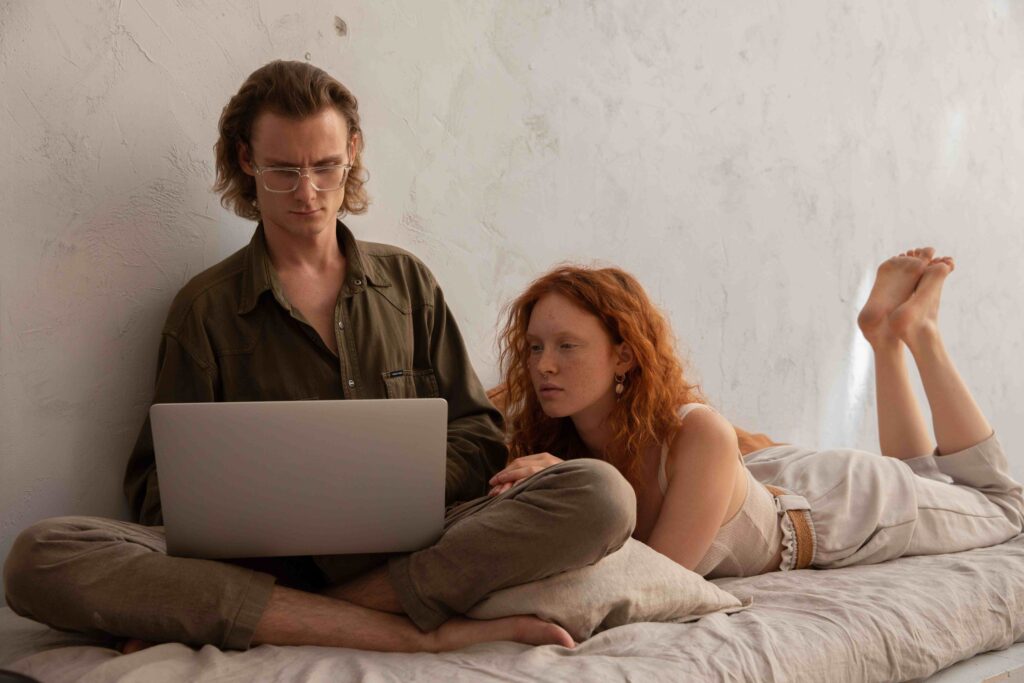 A woman watching her partner work on his laptop exhibiting habits of an overly needy girlfriend.