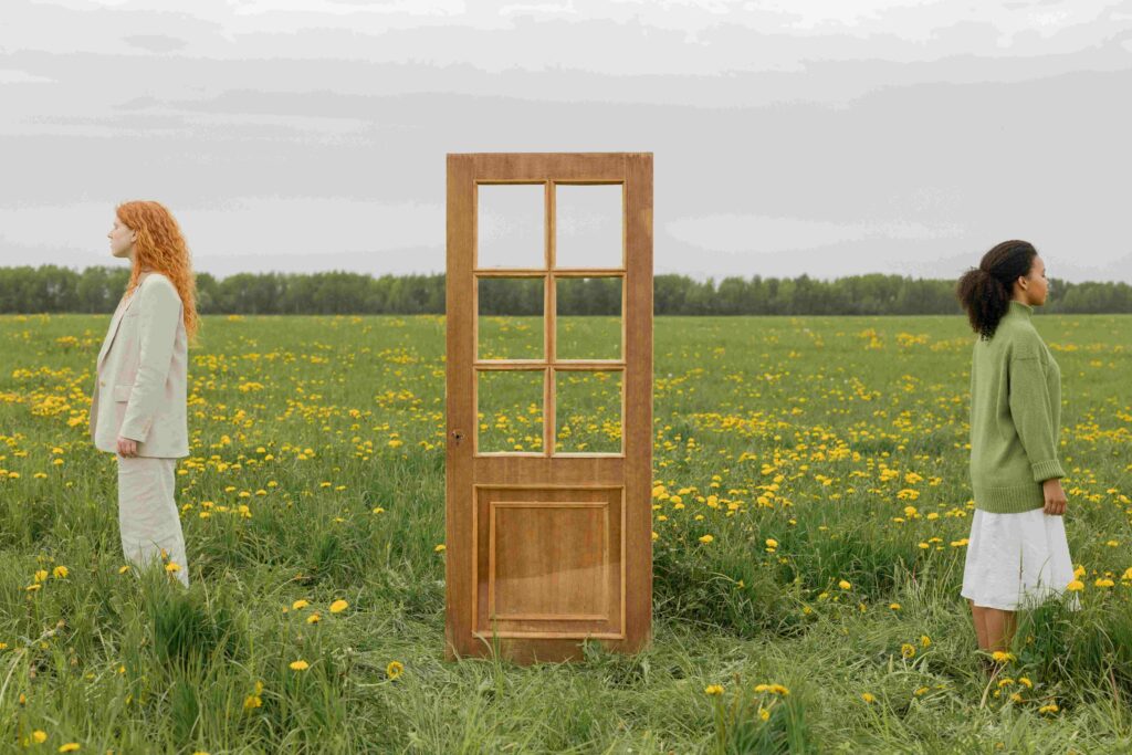 Two people standing on opposite sides of a door in a field illustrating kindred friendship bond.