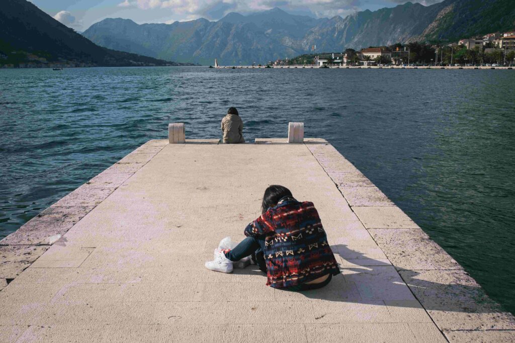A lonely person sitting at the edge of a pier feeling drained by insincere friendships. 