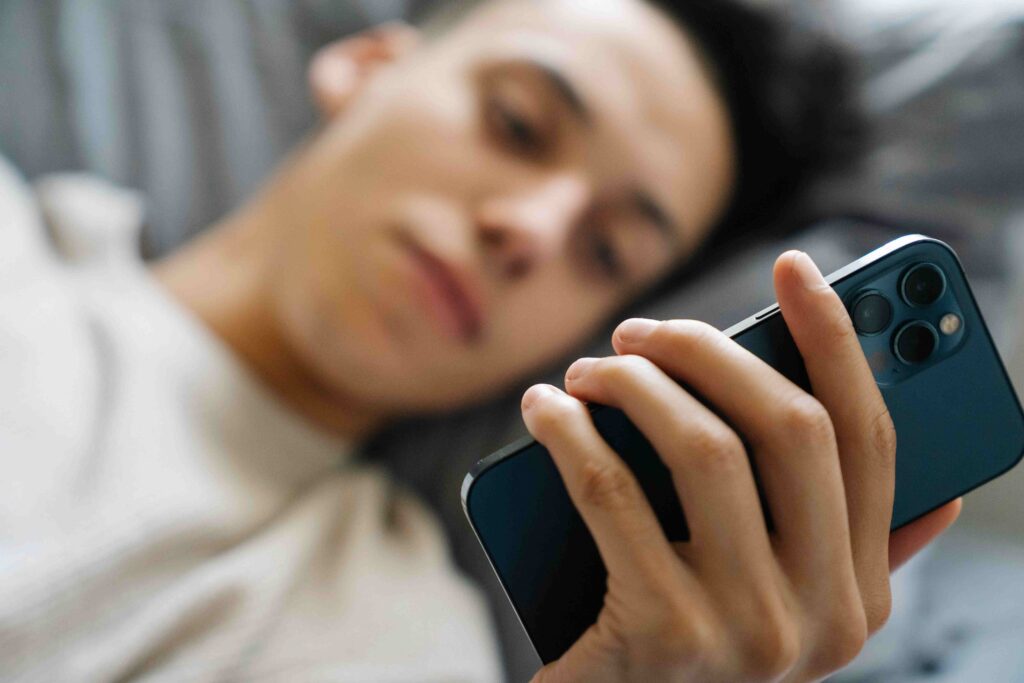 A man lying down holding his smartphone representing an overly dependent boyfriend.
