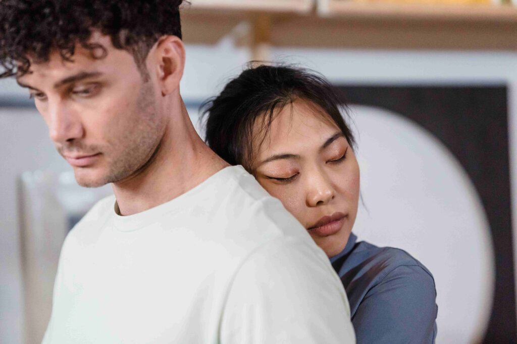 A woman leaning anxiously on her partner's shoulder reflecting the meaning of clingy in a relationship. 