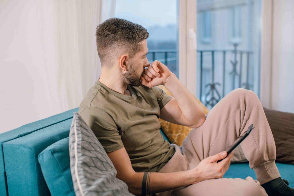 A worried man sitting on a sofa with a phone resolving role confusion in adult relationships.