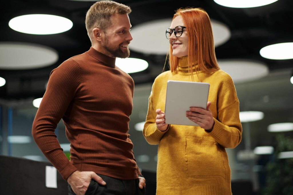 Work Husband Meaning: 7 Rules to Keep It Strictly Platonic Two professional coworkers smiling and talking with tablet discussing work husband concept.