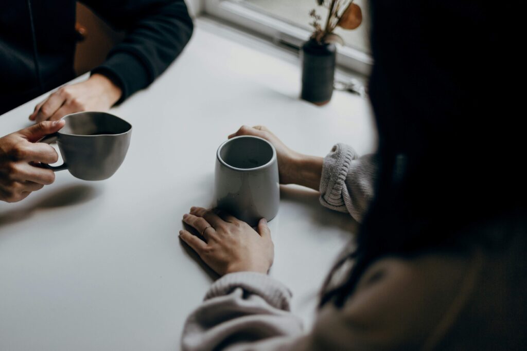 Two partners holding coffee mugs across table practicing reconnecting with partner safely.