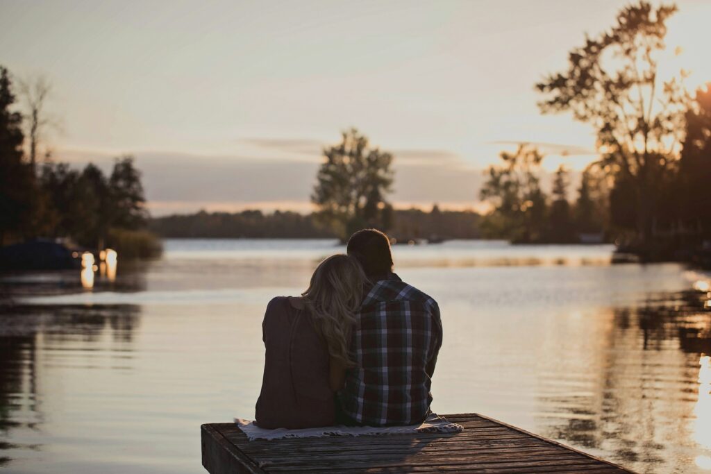 How to Stop Being Emotionally Distant & Reconnect With Your Partner A loving couple sitting on a dock by lake learning how to stop being emotionally distant.