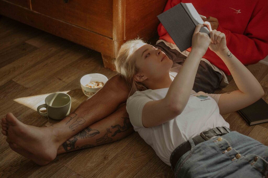 A young woman lying on the floor reading a book with partner practicing a mysterious dating style. 
