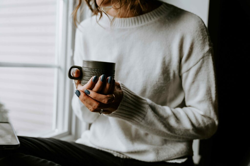 A woman in white sweater holding a warm coffee cup enjoying a self sovereignty lifestyle.