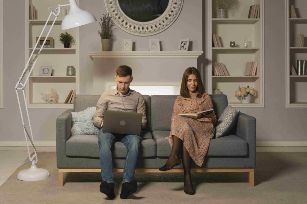 A couple relaxing on sofa doing parallel activities showing independent partner traits. 