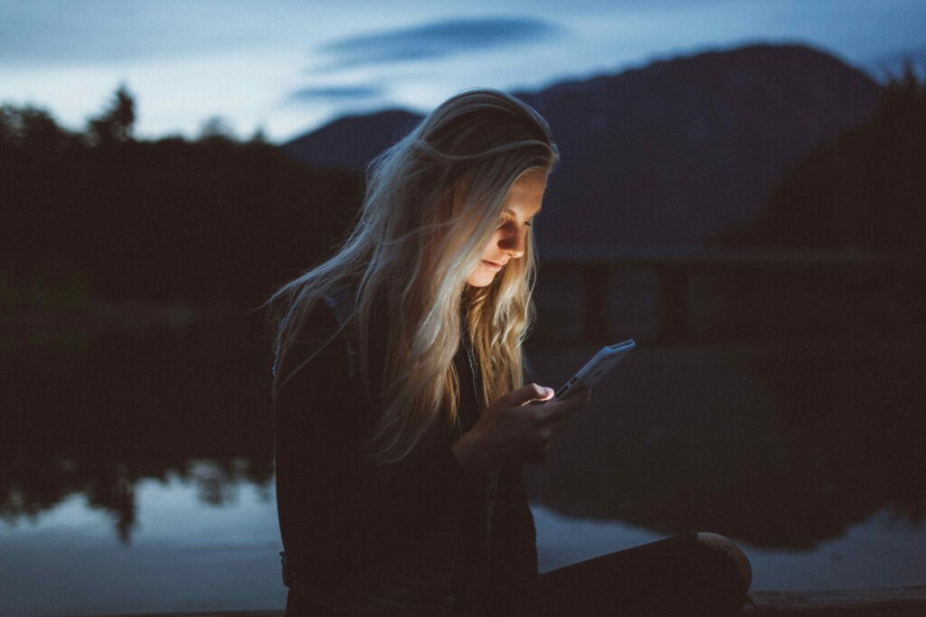 A woman sitting outdoors at night looking at her phone experiencing adult social isolation. 