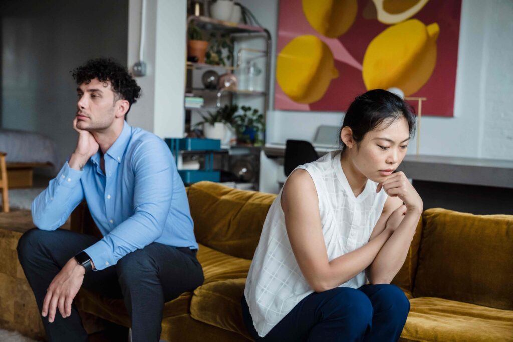 A sad couple sitting distant on couch illustrating relationship anxiety dreams and broken trust.