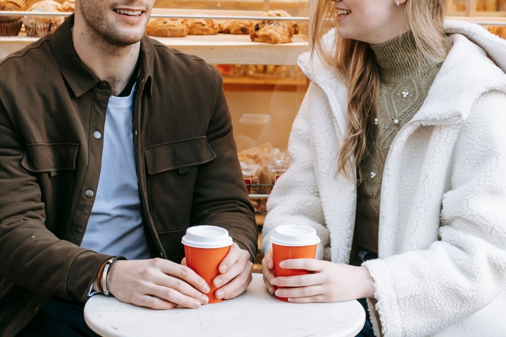 A young man and woman talking with coffee cups in front of a bakery using fast track dating tips.