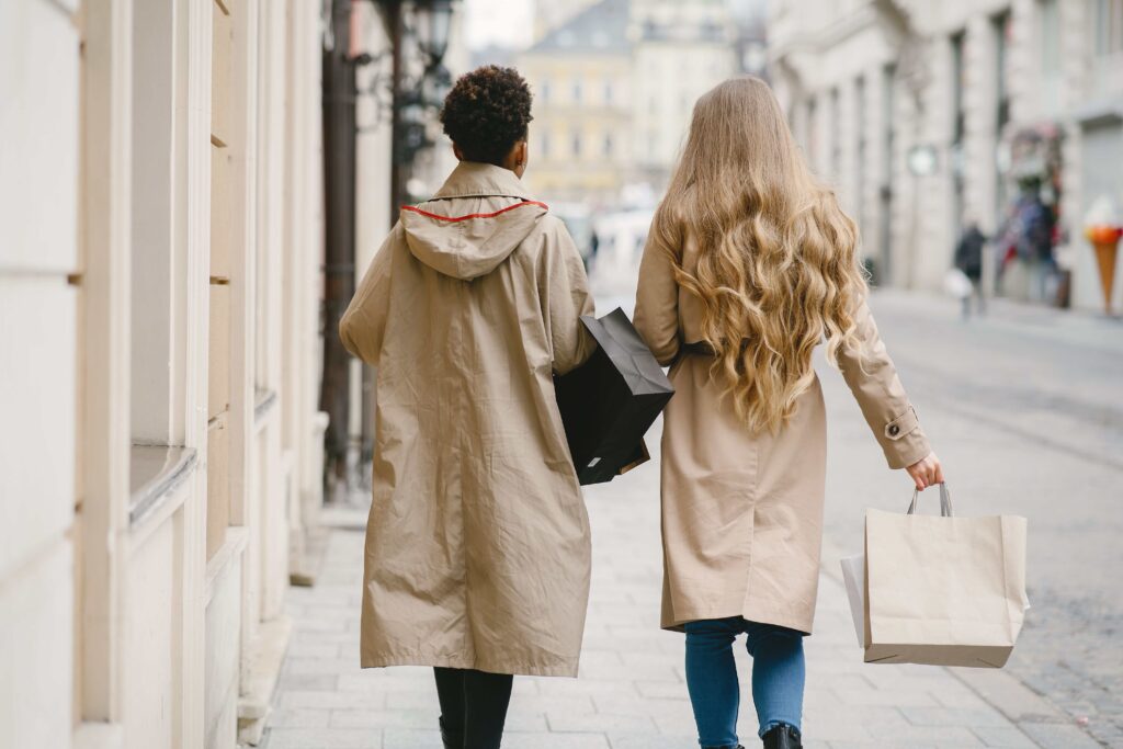 Two women walking along city street holding shopping bags while expanding social circles.