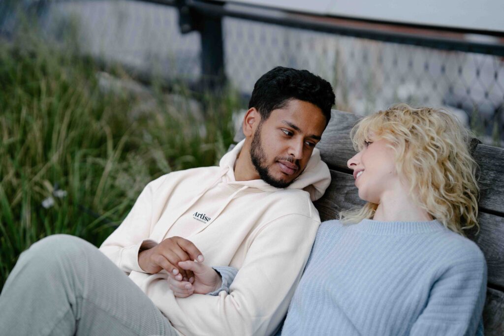 A couple sitting close on a wooden bench practicing rebuilding trust after breach.