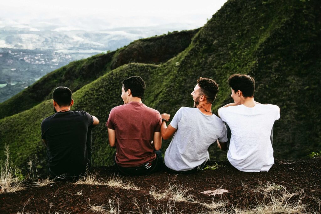 Four male friends sitting together on grassy mountain ridge building adult friendships.
