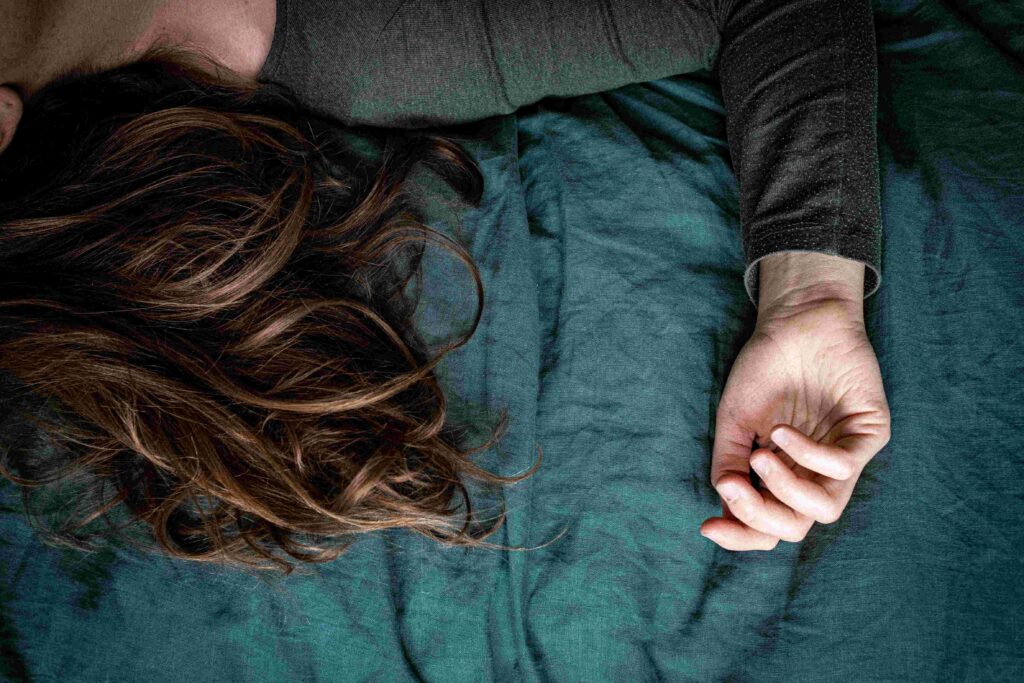 9 Types of Dreams in Psychology (& Why You See Your Ex) A woman sleeping with hair spread out on dark bed exploring different types of dreams.