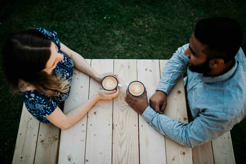 Top view of a man and woman holding coffee cups at a wooden table during quick dating events.